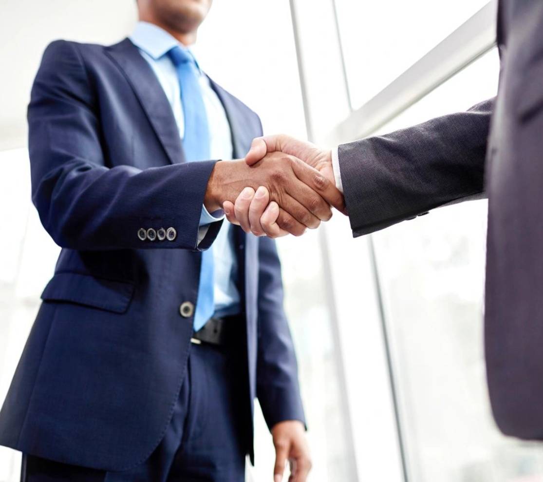 Two men in suits shaking hands over a window.